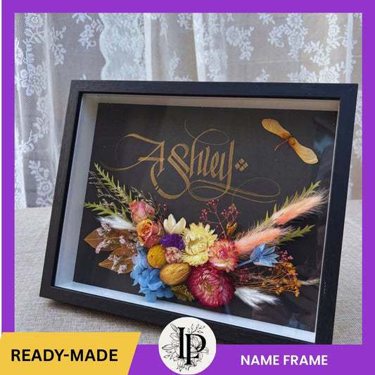 Decorative name frame with colorful flowers and feathers on a dark background, featuring the name 'Ashley'.