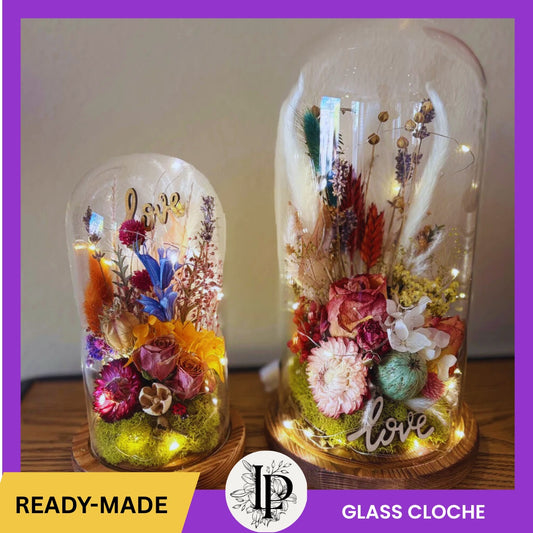 Two glass cloches with floral arrangements and 'love' text on a wooden surface.