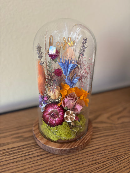 Glass dome with preserved flowers on a wooden base against a plain background