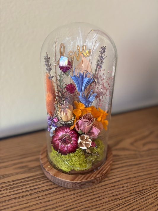 Glass dome with preserved flowers on a wooden base against a plain background