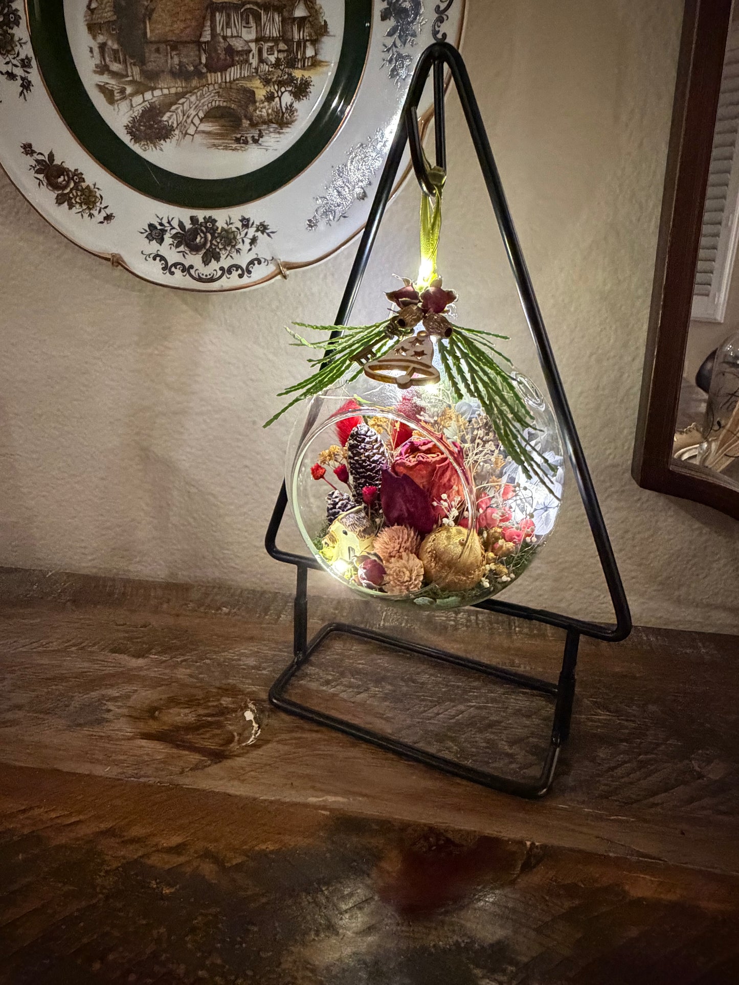 Decorative glass sphere with plants on a stand against a wall with a decorative plate.