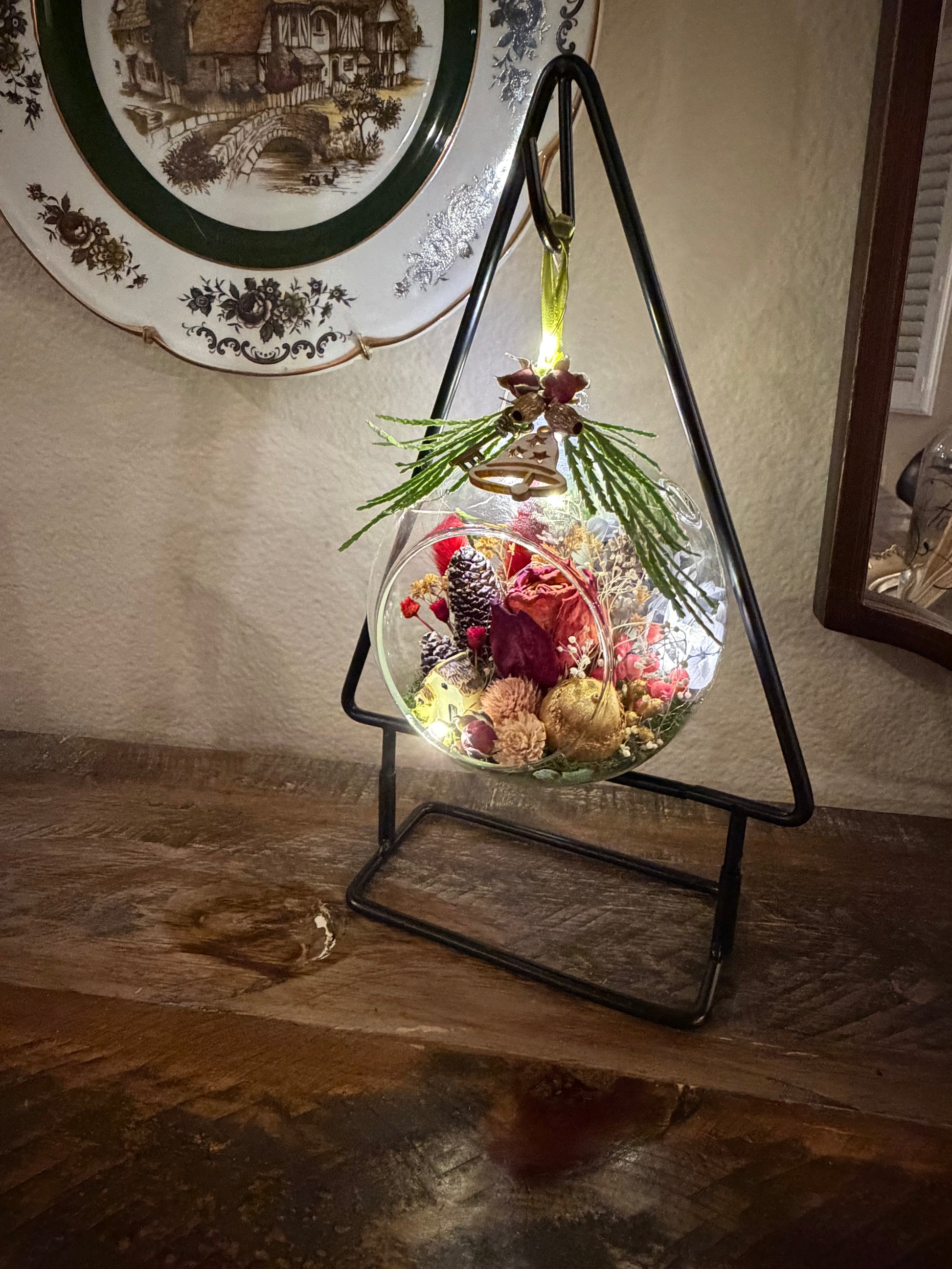 Decorative glass sphere with plants on a stand against a wall with a decorative plate.