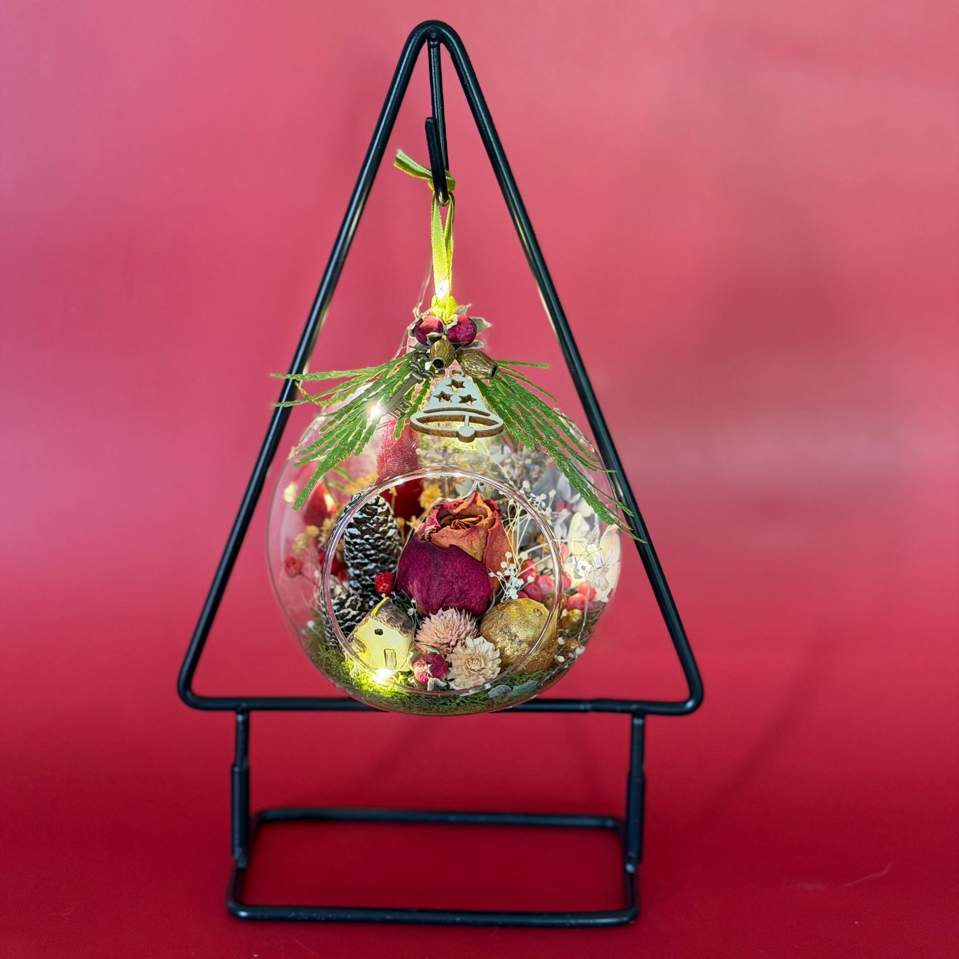 Decorative glass ball with lights and natural elements on a black stand against a red background