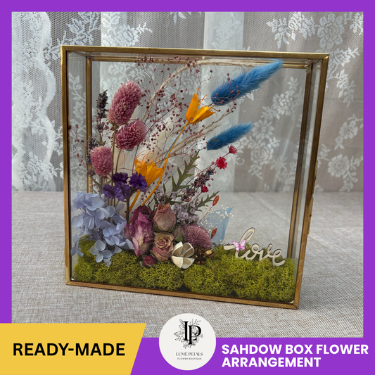 Decorative shadow box with pressed flowers and the word 'love' on a textured surface.